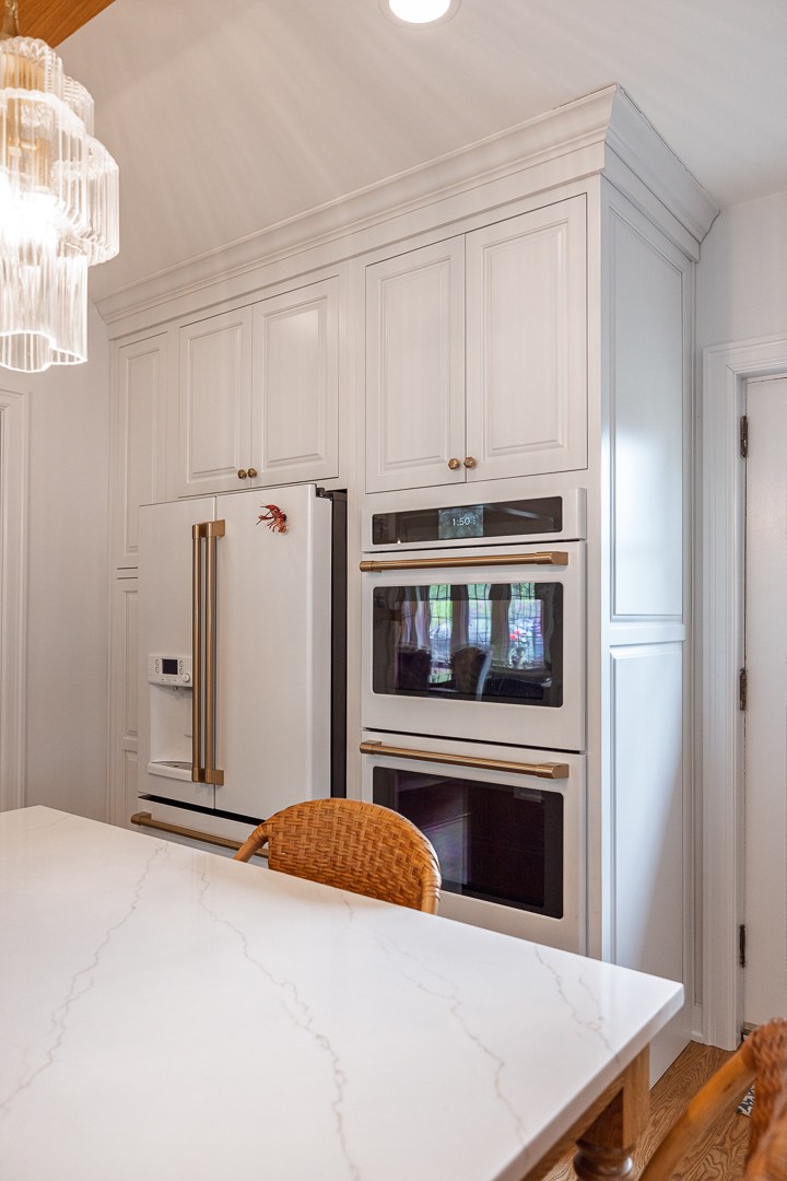 Cincinnati kitchen with white cabinetry, built-in double ovens, paneled refrigerator, and brass hardware in a bright, modern space