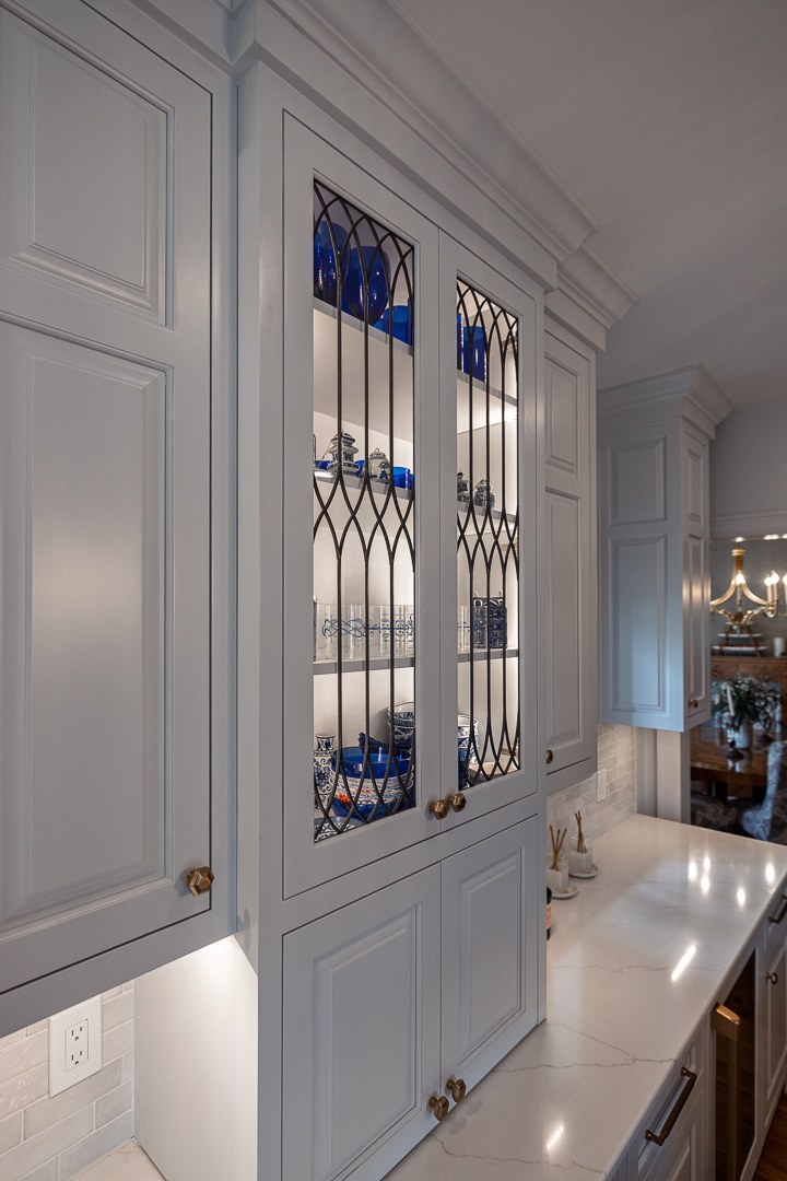 Cincinnati kitchen with white glass-front cabinetry, brass knobs, and display shelves showcasing dishware in a bright, elegant space