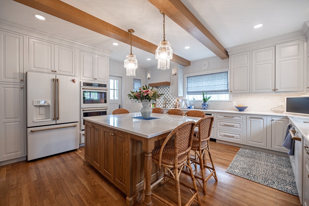 Cincinnati kitchen with wood island, white cabinetry, woven stools, pendant lights, exposed beams, and stainless appliances in a bright open layout