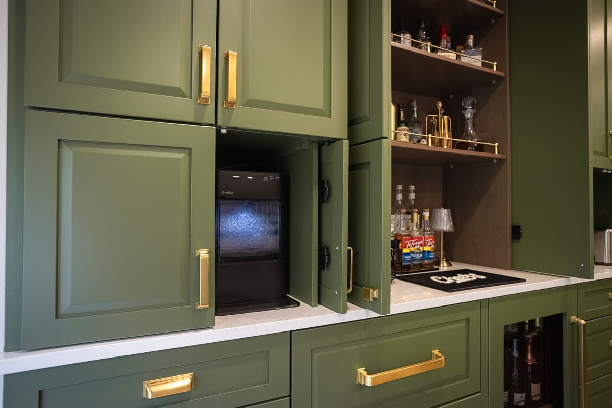 Custom green cabinetry with brass pulls, built-in beverage station, coffee maker, open shelving, and wine fridge.