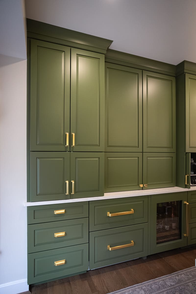 Floor-to-ceiling green kitchen cabinetry with quartz counter, brass hardware, drawers, and built-in beverage fridge.