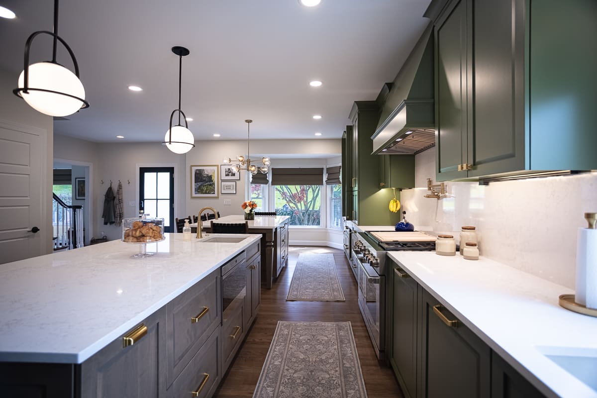 Galley view of remodeled kitchen with green cabinetry, stainless steel range, quartz countertops, and brass hardware.