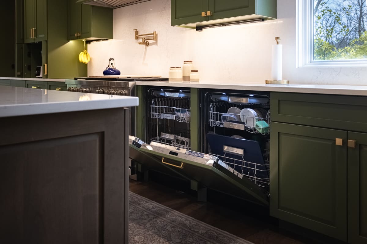 Green kitchen cabinetry with quartz countertops, brass hardware, stainless range, and two built-in dishwashers.