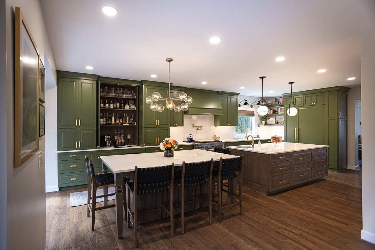 Open-concept kitchen remodel with green cabinets, dual islands, quartz countertops, brass hardware, and dining area. Open-concept kitchen remodel with green cabinets, dual islands, quartz countertops, brass hardware, and dining area.