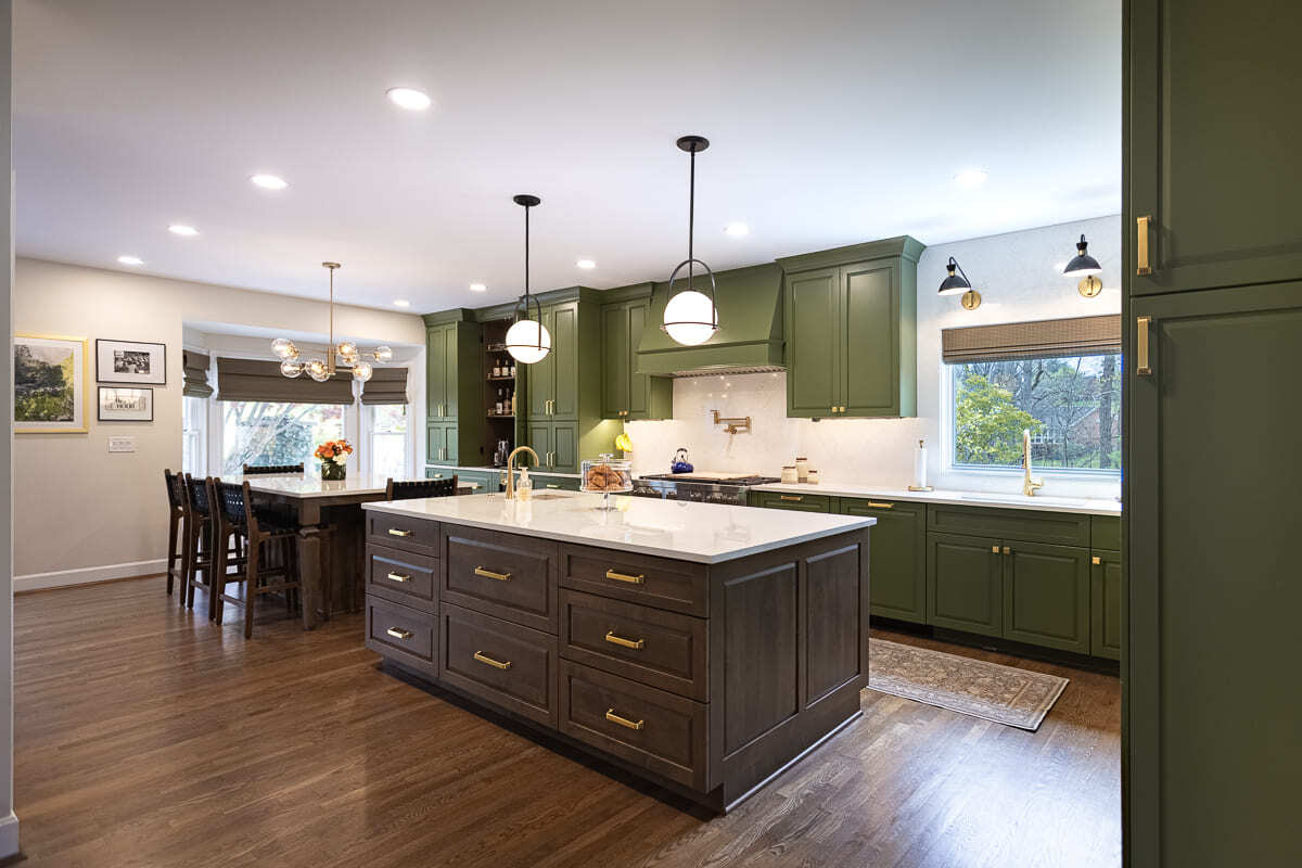 Remodeled kitchen with green cabinetry, large wood island, quartz countertops, brass fixtures, and pendant lighting.