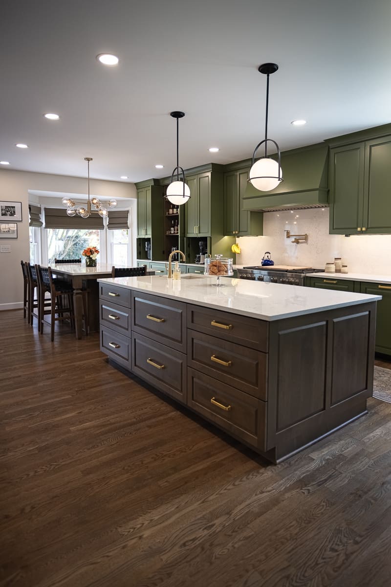 Spacious remodeled kitchen with green cabinetry, dark wood island, quartz countertop, brass pulls, and pendant lights.