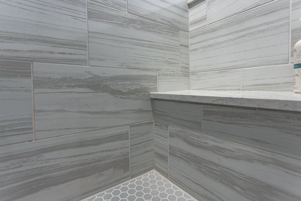 Close up of shower tiles with large format wall tiles and small hexagonal floor tiles and seating