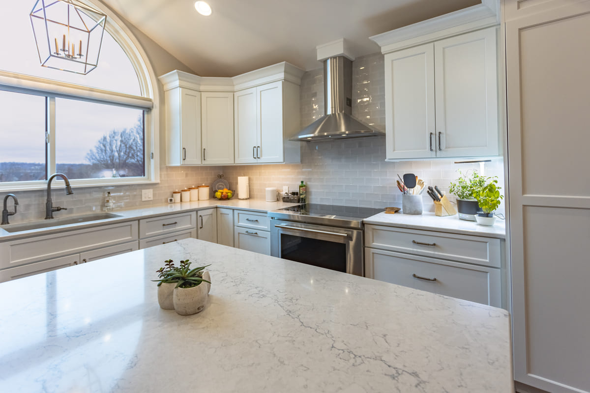 Open-concept kitchen designed by Legacy Builders with stone countertop island and arched window above sink