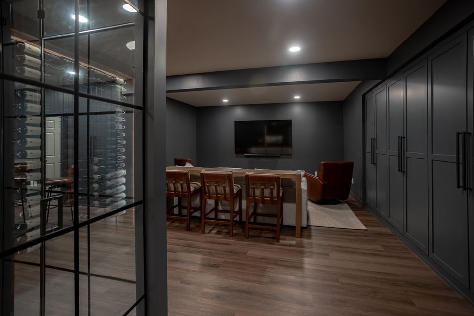 Finished basement with wood flooring, glass wine storage, dark cabinetry, lounge seating, and a wall-mounted TV.