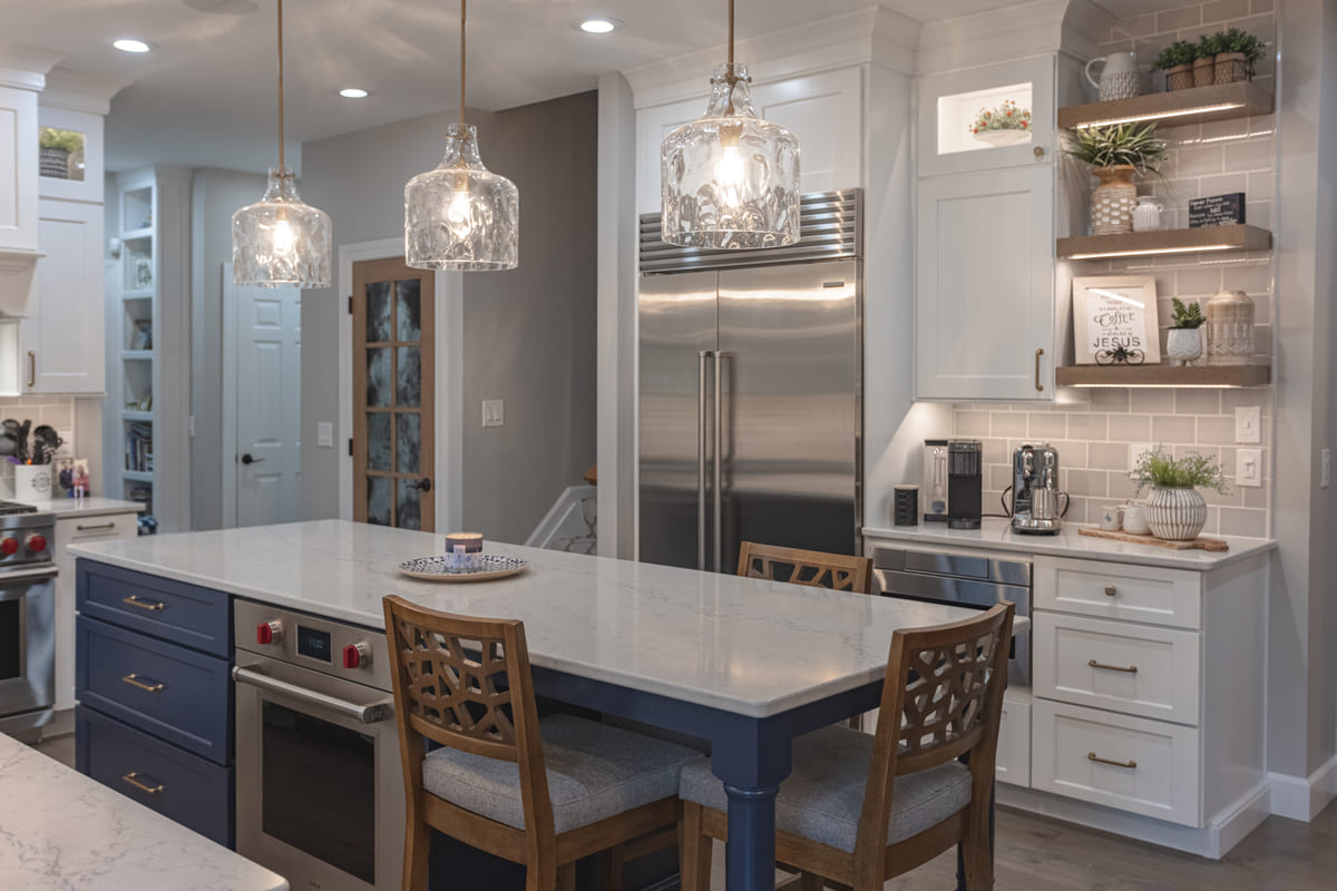 Kitchen island with seating, oven, and pull-out cabinetry beneath three pendant glass light fixtures