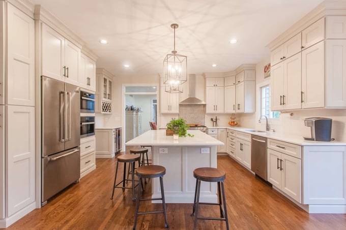 White kitchen remodel with island and barstools beneath pendant lighting by Legacy Builders Group