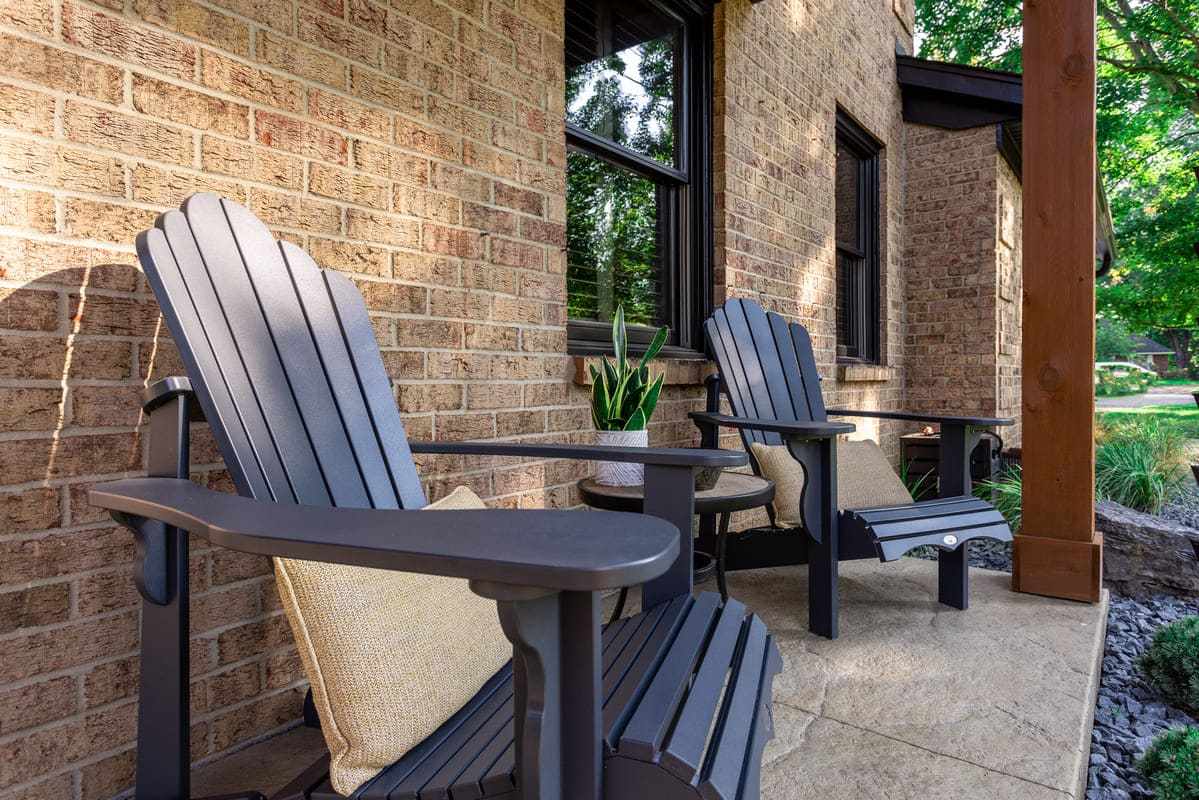 Two Adirondack chairs on porch of brick homea