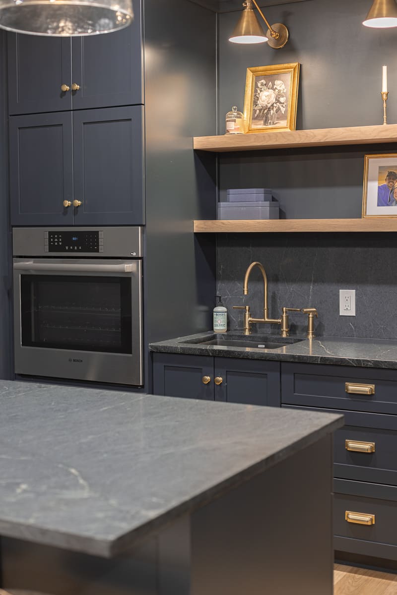 Dark built-in bar with navy cabinetry, stone countertops, brass fixtures, and open shelving in a Cincinnati basement Dark built-in bar with navy cabinetry, stone countertops, brass fixtures, and open shelving in a Cincinnati basement