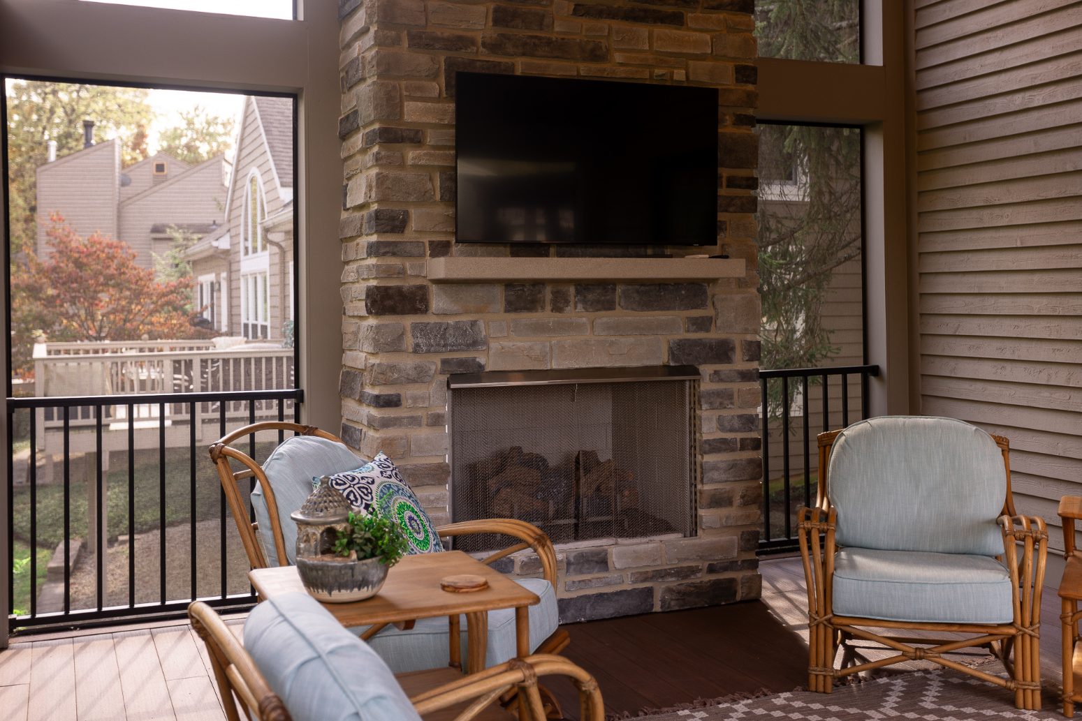 Stone fireplace with chairs in front and mounted TV in screened-porch addition by Legacy Builders