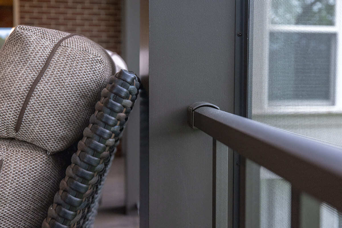Close-up of screened outdoor deck railing, dark post, mesh screen, and wicker lounge chair.
