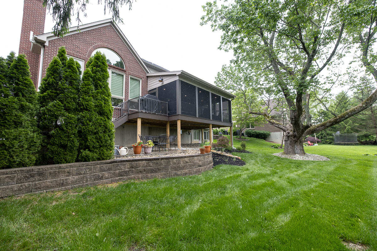 Outdoor living remodel with screened deck, wood posts, backyard patio, and mature trees.