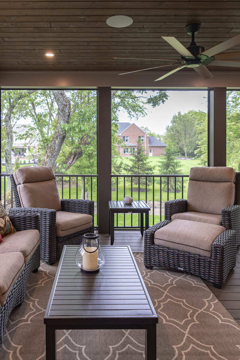 Screened deck seating area with wicker chairs, wood coffee table, ceiling fan, and outdoor views.